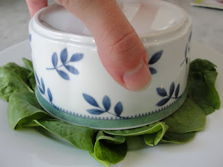 hand holding small bowl tipped upside down on bed of lettuce