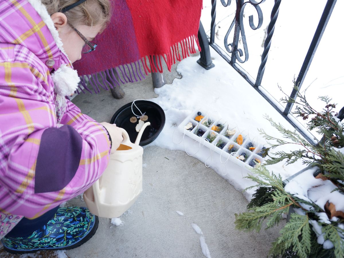 child pouring water into ice cube tray outside on snowy porch to make ice ornaments