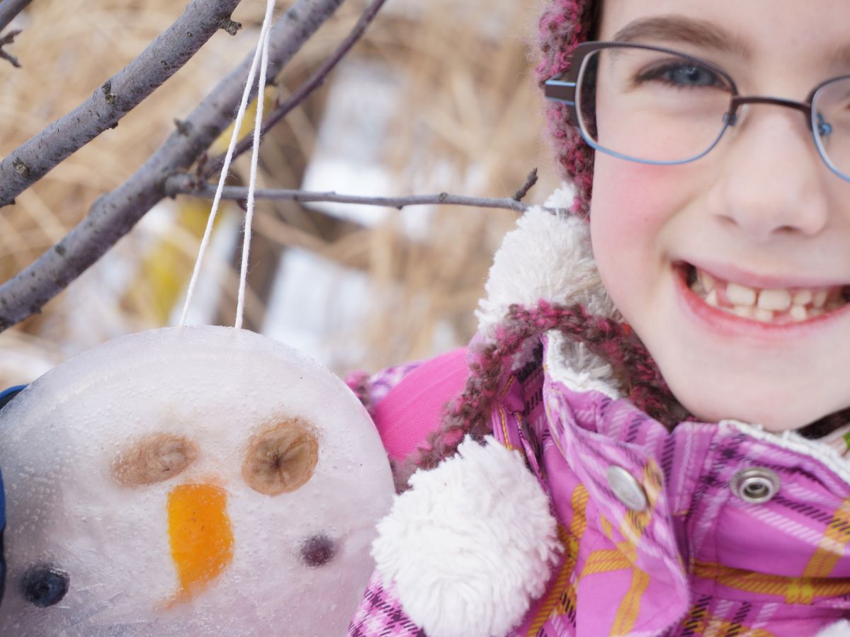 girl holding round ice ornament she made with a banana and orange peel face