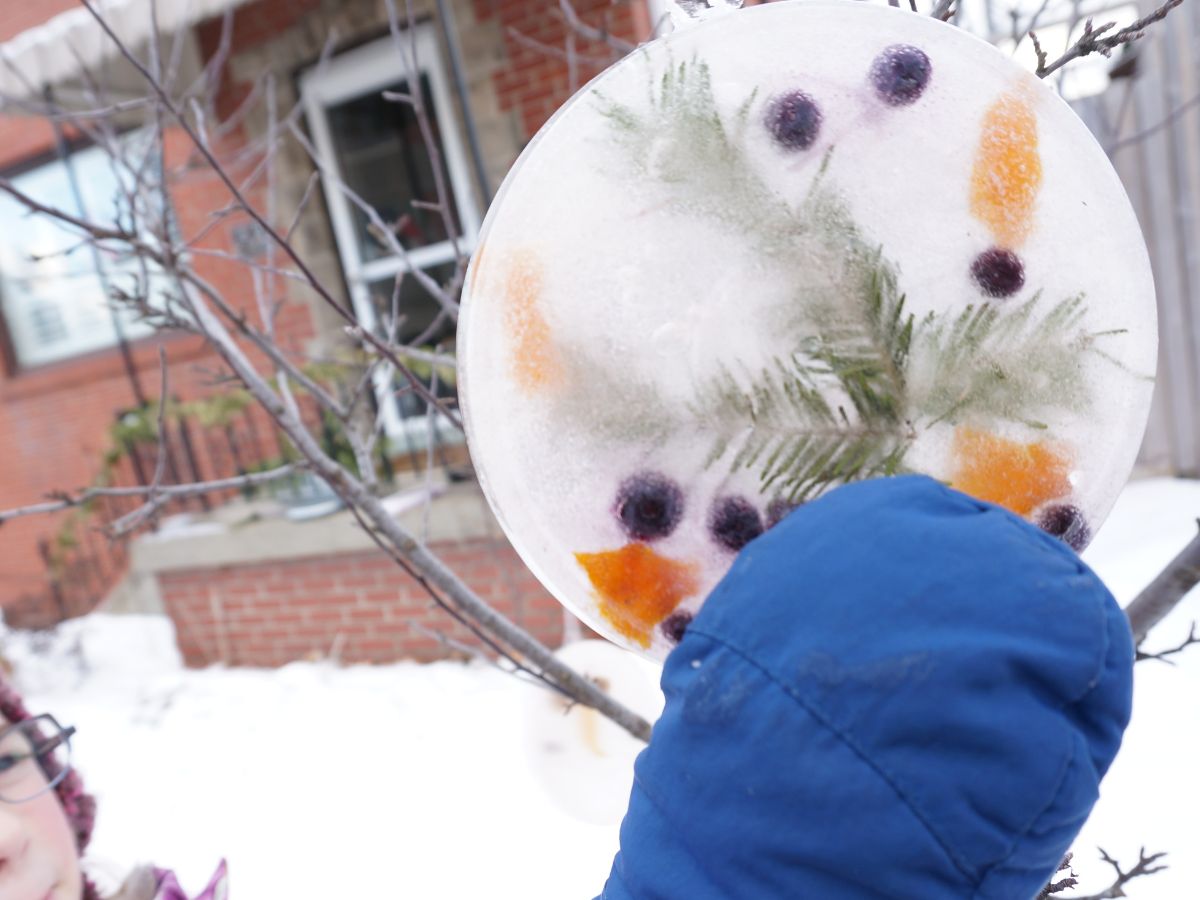 mitten hand holding round ice ornament hanging from tree