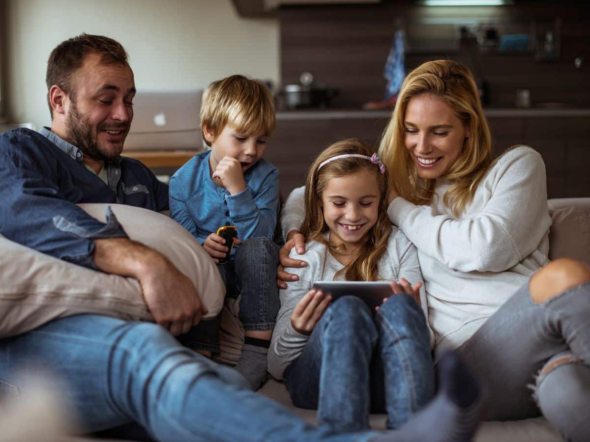 family of four watching movie on a device sitting on a couch in a hotel room