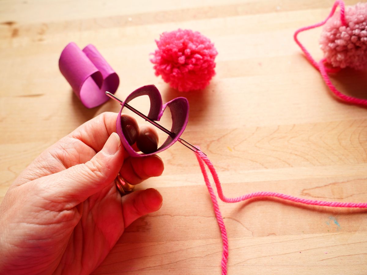 toilet roll heart in woman's hand with embroidery needle with yarn being fed through it