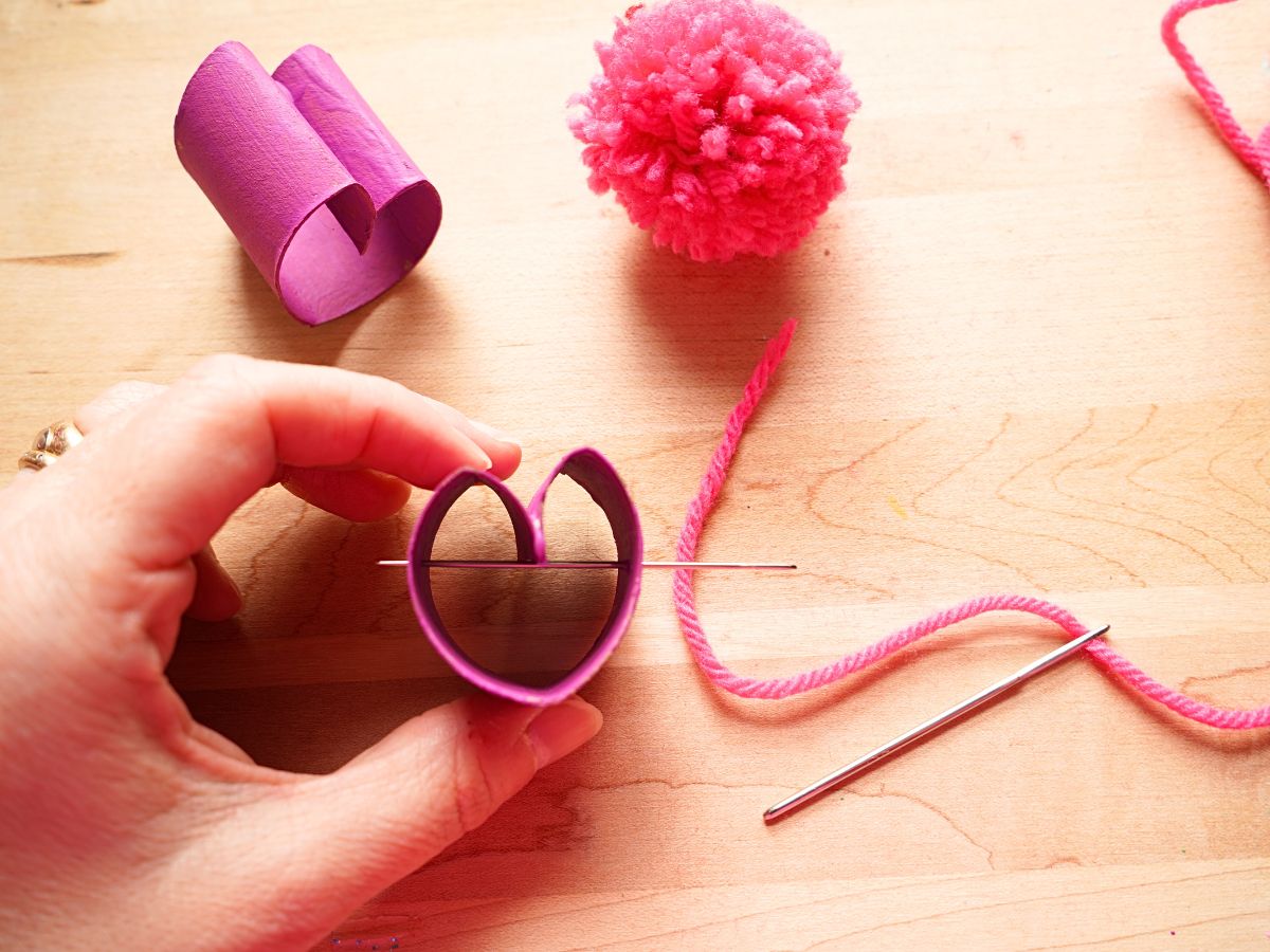 toilet roll heart with sharp embroidery needle poked through it being held in woman's hand