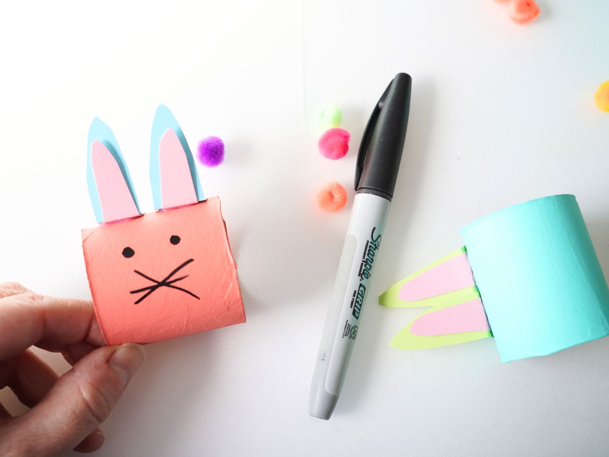 close up of black marker drawing a bunny face on toilet roll napkin ring